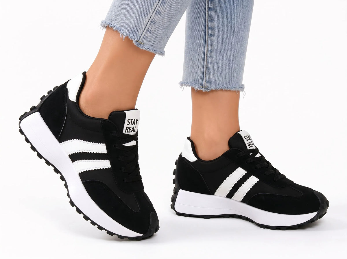Black trainers with white stripes and chunky platform soles, worn mid-stride with light jeans on a white background 19
