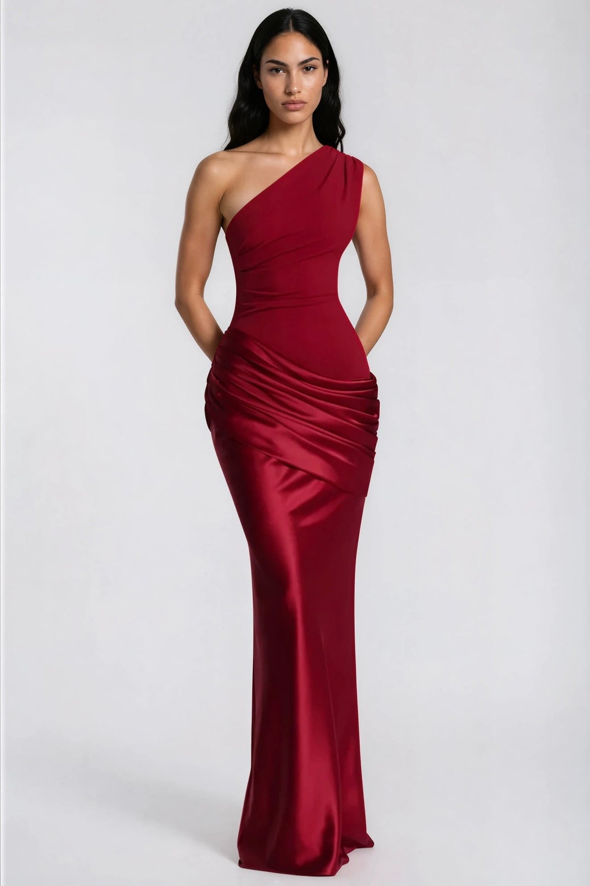 Front view of the deep red one-shoulder maxi dress with hands behind the back, showing the draped satin waist and sleek skirt. 37