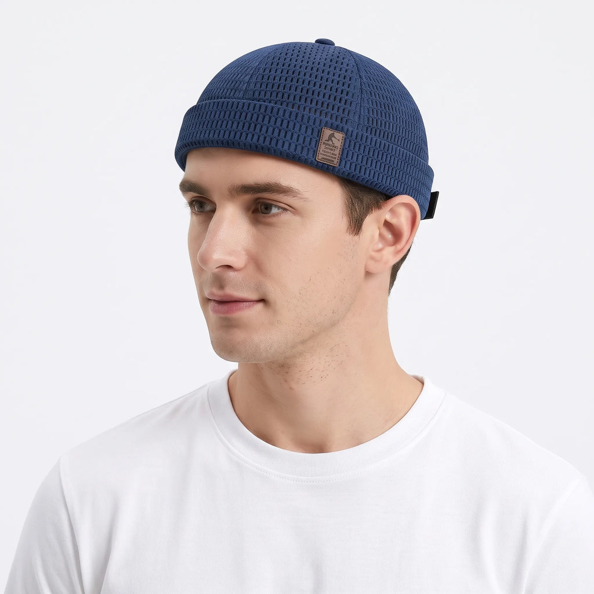 Man in a white t-shirt wearing the navy blue open weave brimless cap, turned slightly left 25