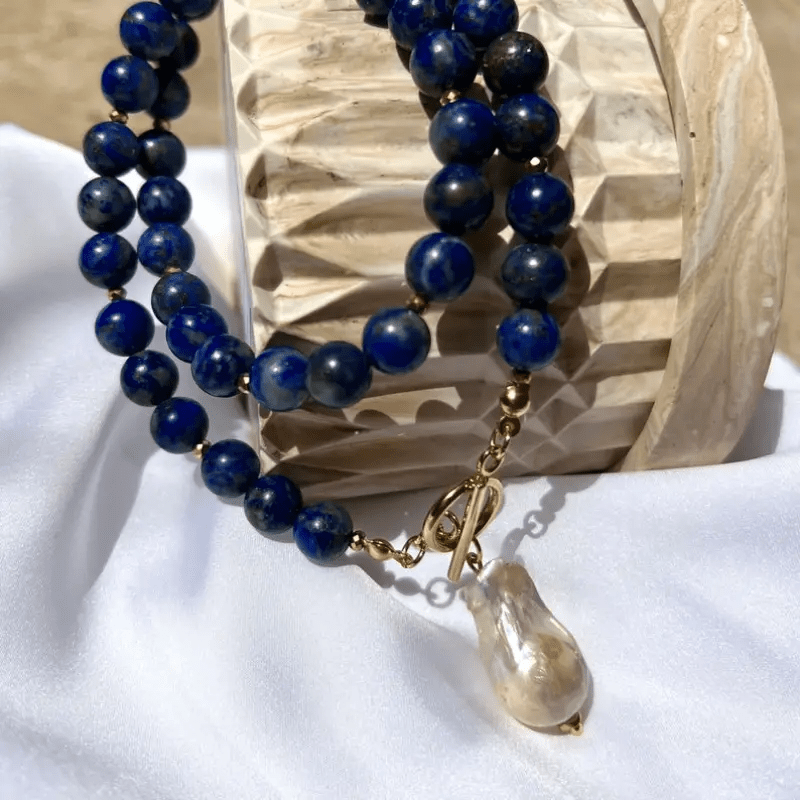 Blue beads looped over a carved wooden block on white fabric, pearl pendant hanging below 9