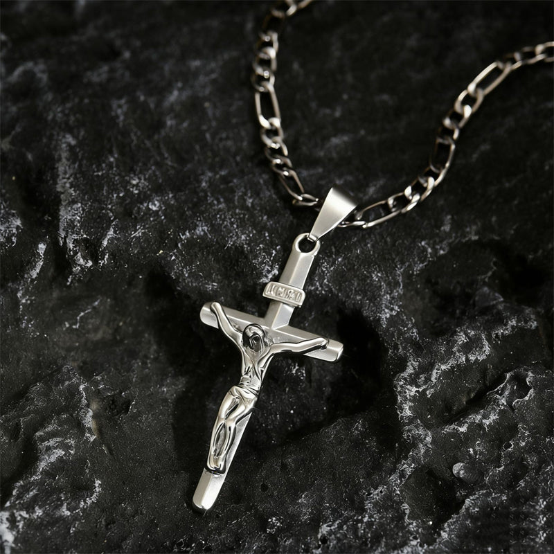 Silver-tone crucifix pendant with INRI plaque and Figaro chain resting on dark textured rock 10