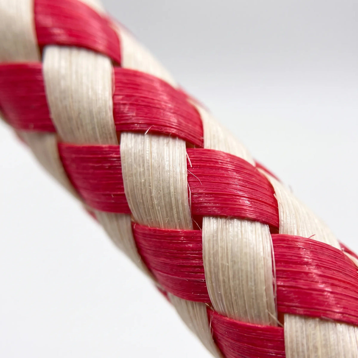 Close-up of the woven strips on a red and cream finger trap, showing the tight diagonal weave and fibrous texture. 3