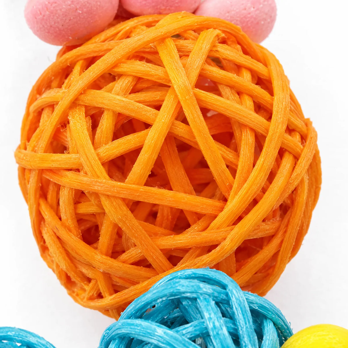 Close-up of an orange woven rattan ball with pink and blue pieces beside it, showing the texture of the strands. 3