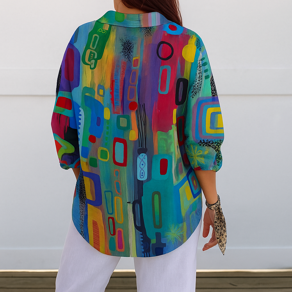 Back view of the blouse on a model, showing the continuous multicoloured abstract print, rounded hem and three-quarter sleeves with white trousers. 7