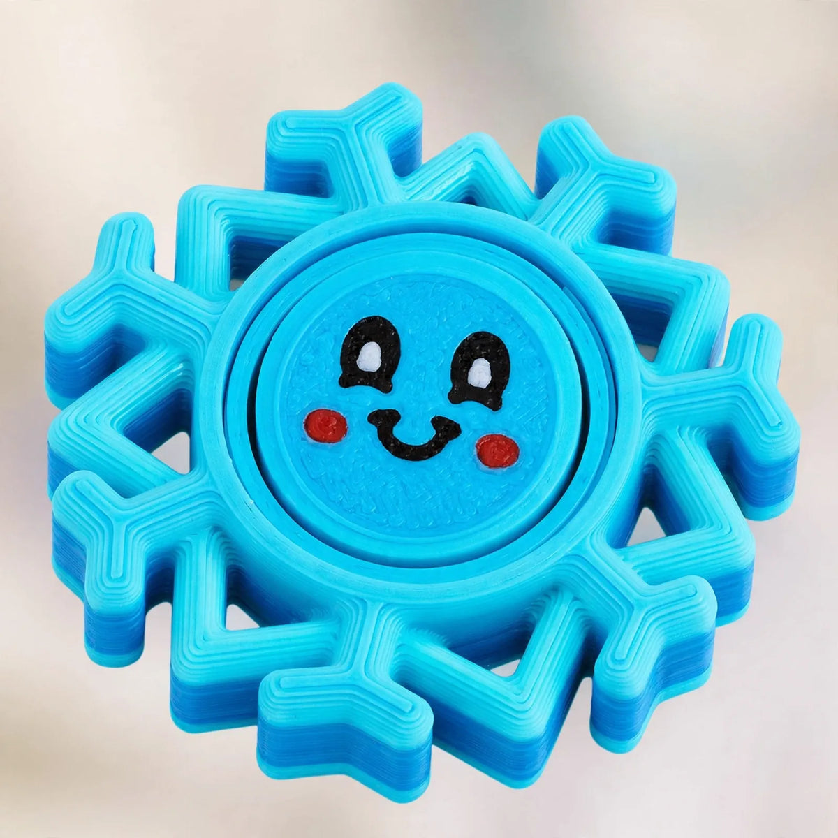 Close-up of a blue 3D printed snowflake spinner with a smiling face and visible layer lines 3