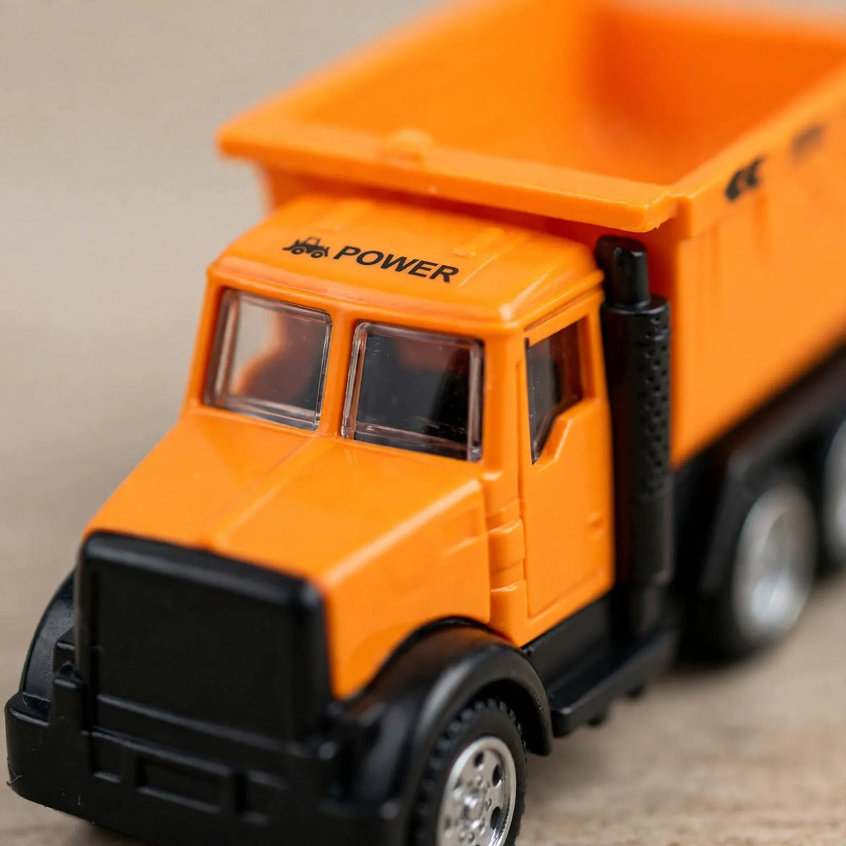 Close-up of an orange toy dump truck cab with black bumper and clear windows 3