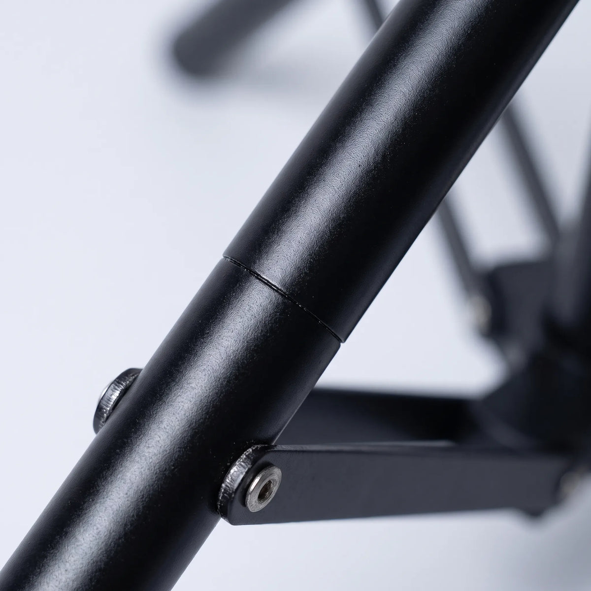 Close-up of a matt black tripod leg showing the tube joint and a metal screw fixing the folding brace. 3