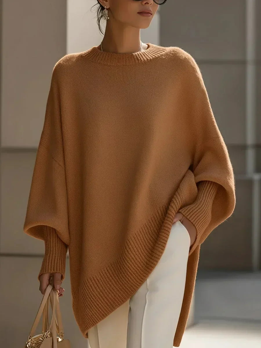 Camel brown version of the oversized jumper on a model, showing the ribbed hem and cuffs with white trousers. 12