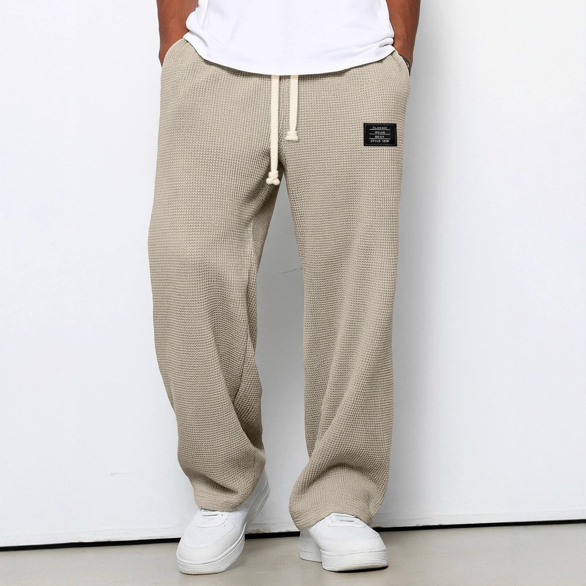 Slightly closer front view of the trousers in beige on a model, showing the cream drawstring, hip patch and relaxed wide legs. 6
