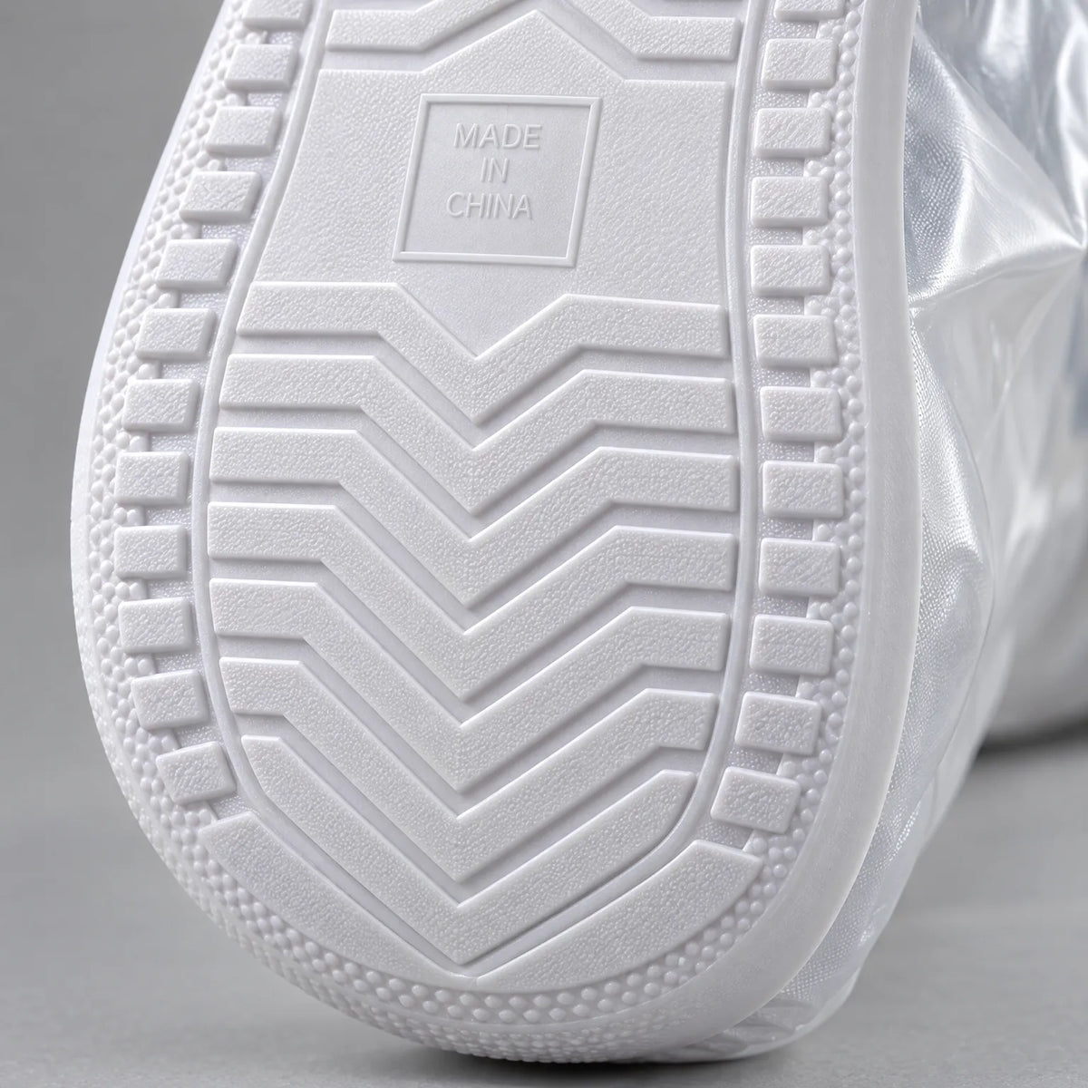 Close-up of the white non-slip chevron-patterned sole of an overshoe, with a small embossed square and a textured edge. 6