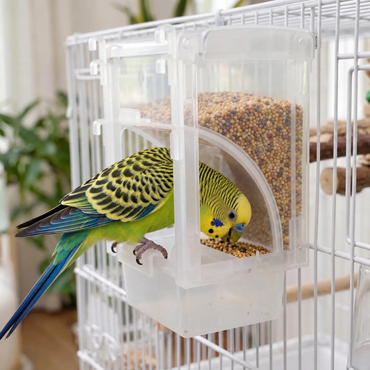 Budgerigar with yellow and green plumage perched on the feeder tray, eating seed from the clear hopper hung on a white cage. 2