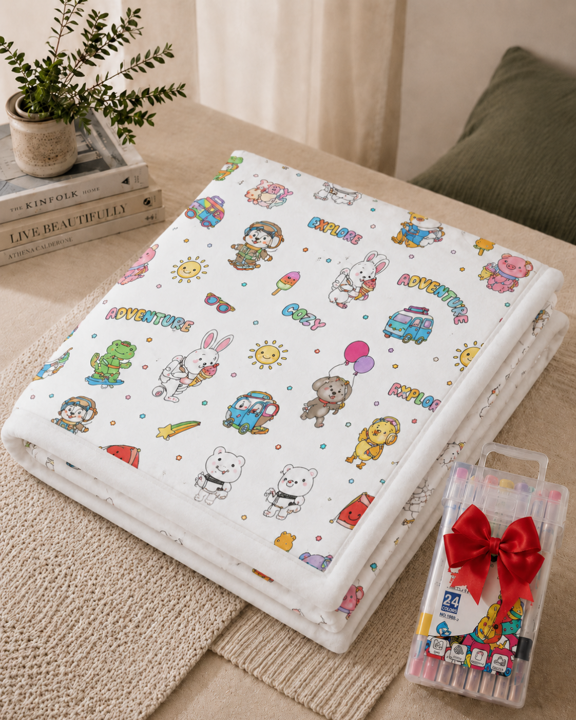 Folded white blanket printed with partly coloured cartoon animals, vans and suns, next to a boxed marker set 10