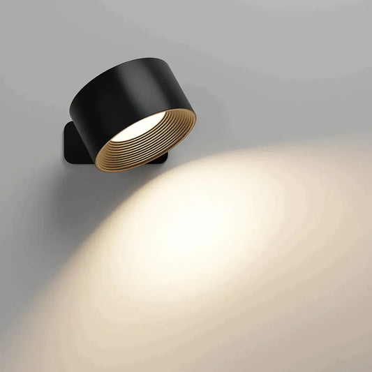 Black version of the wall light with a ribbed inner ring, lit and throwing a soft glow down the wall. 2