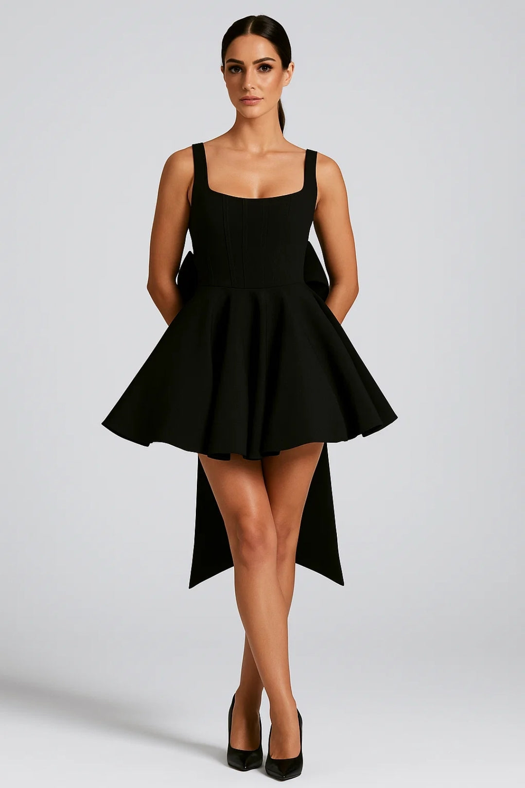 Model wearing the dress in black, front view, with long bow tails at the back and black heels 8