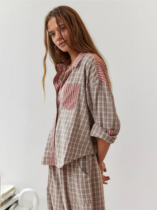 Model in the pink and beige check pyjama set with striped pocket and collar, turned side-on with one sleeve rolled up. 2