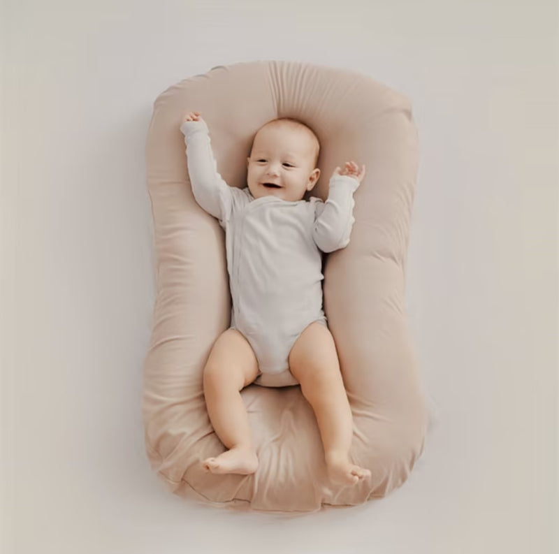 Overhead view of a baby with raised arms on a soft beige cushion 7