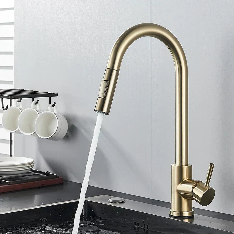 Brushed gold kitchen tap with arched spout and side lever, water running into a dark sink beside hanging white mugs. 6