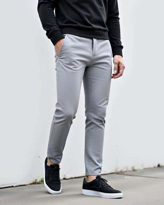 Light grey chinos worn with a black sweatshirt and black trainers, model standing in front of a white wall outdoors. 2
