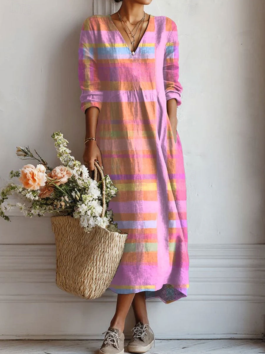 Model wearing a long-sleeved, V-neck midi dress in pink, orange and blue stripes, one hand in a pocket, carrying a flower-filled straw bag. 1