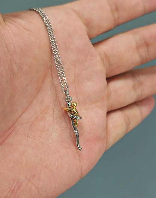 Close-up of the pendant and chain resting on an open palm, showing the small size of the silver and gold-tone hugging figures. 7