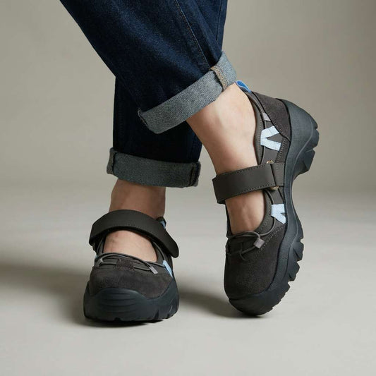 Studio shot of charcoal suede shoes worn with cuffed jeans, showing the grey strap, light blue lacing accents and thick black tread. 2