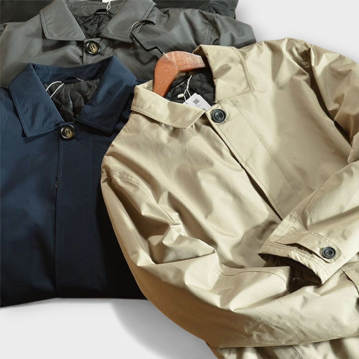 Flat lay of three coats in beige, navy and grey, showing collars, black buttons and quilted lining at the neck. 9