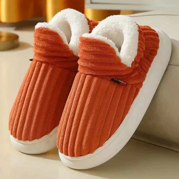 Pair of burnt orange ribbed plush slippers with fluffy white lining and chunky white soles, resting by a sofa. 6