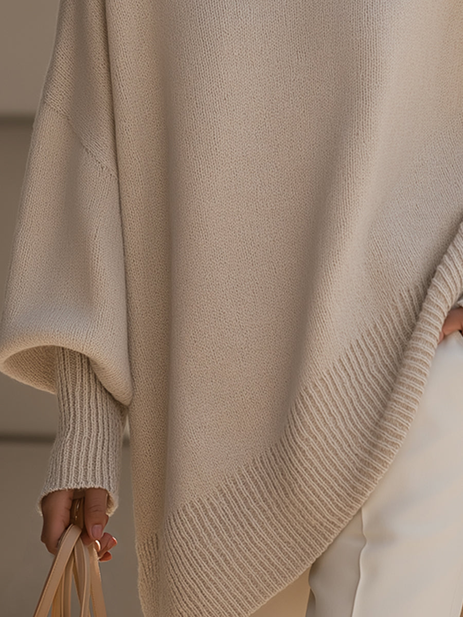 Detail of the cream poncho's ribbed asymmetric hem and ribbed cuff, with a handbag held below 4