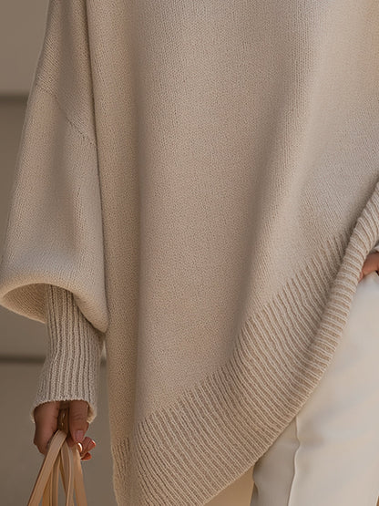 Detail of the cream poncho's ribbed asymmetric hem and ribbed cuff, with a handbag held below 4