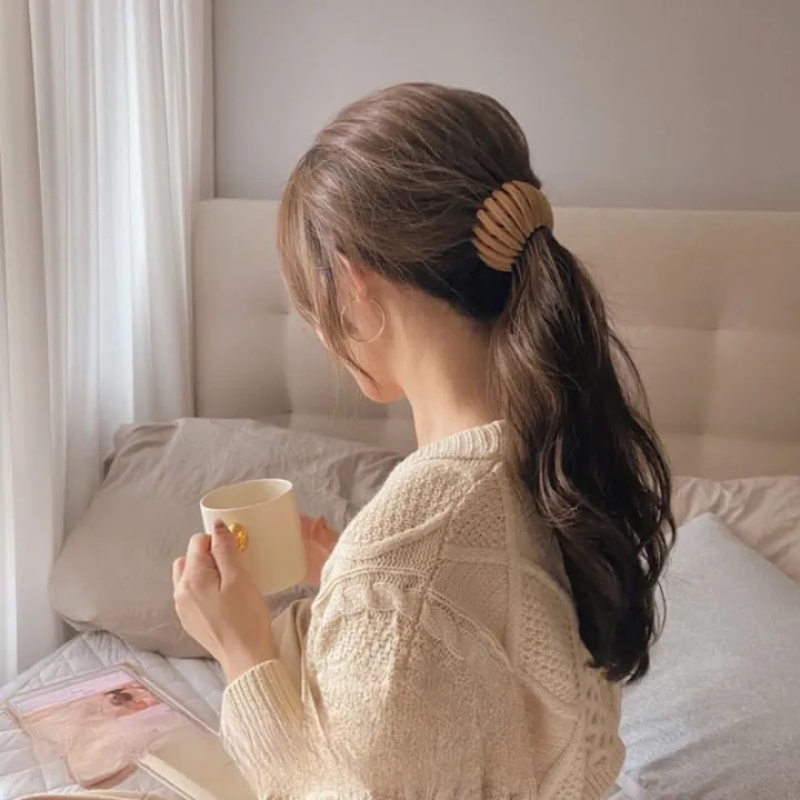 Woman seen from behind in a cream knit jumper holding a mug, wearing a tan ridged clip at her low ponytail. 2