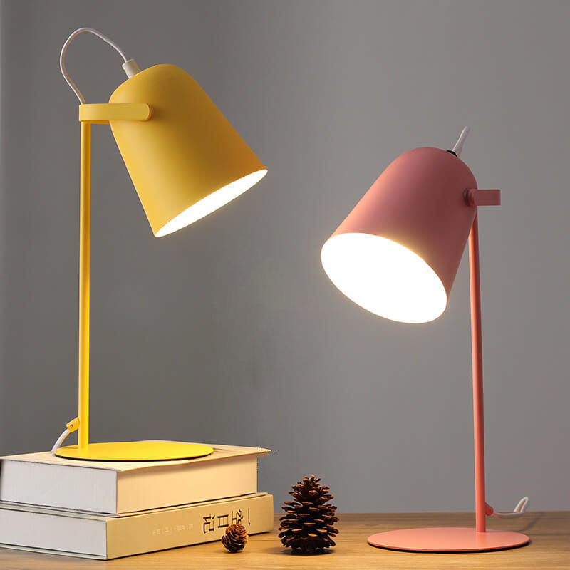 Yellow and pink versions of the lamp lit side by side on a wooden shelf with books and pine cones. 5
