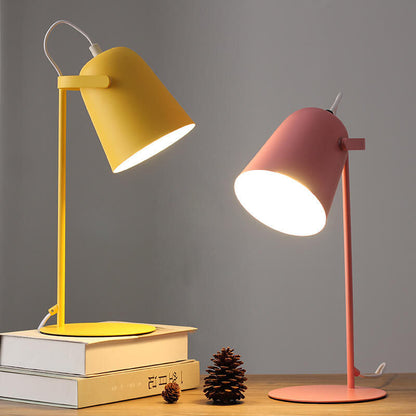 Yellow and pink versions of the lamp lit side by side on a wooden shelf with books and pine cones. 5