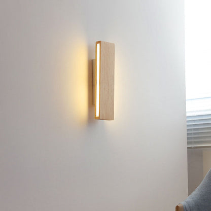 Illuminated vertical wooden bar light on a white wall near a window blind and a grey armchair. 15