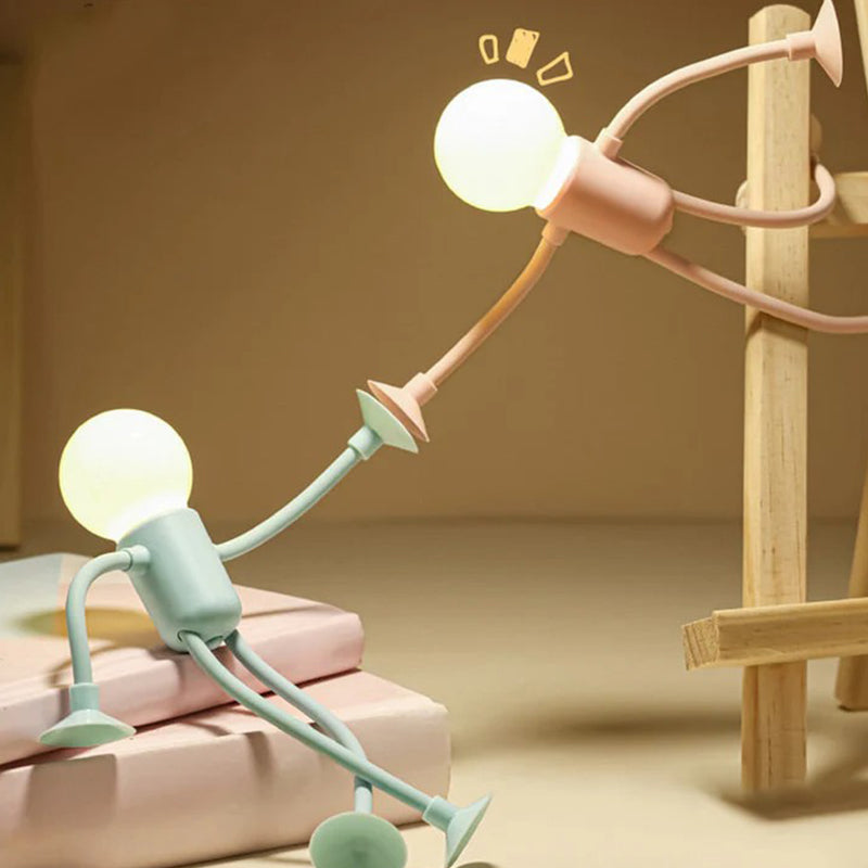 Green figure lamp sits on a pink book stack while a pink one stretches towards it from a wooden frame. 6
