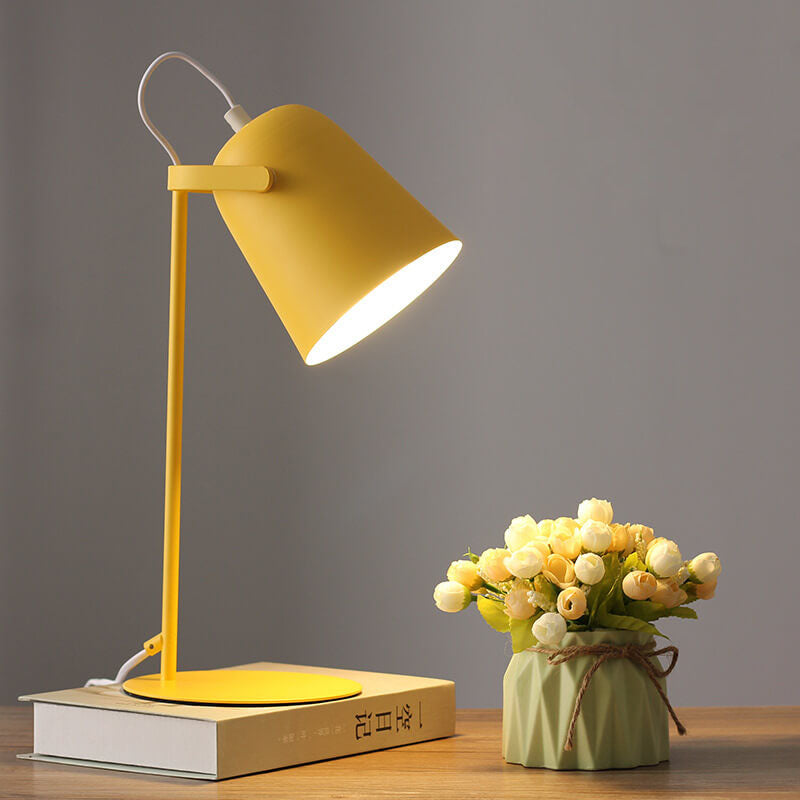 Yellow bucket-shaped table lamp lit on a hardback book beside a small vase of cream artificial roses. 1