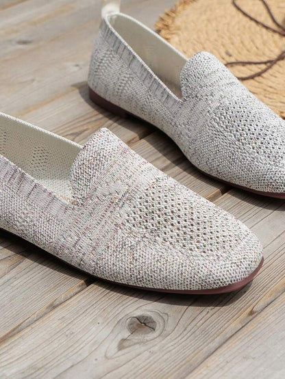 Close-up of light grey knit slip-ons on wooden boards, showing the speckled texture and perforated toe area. 16