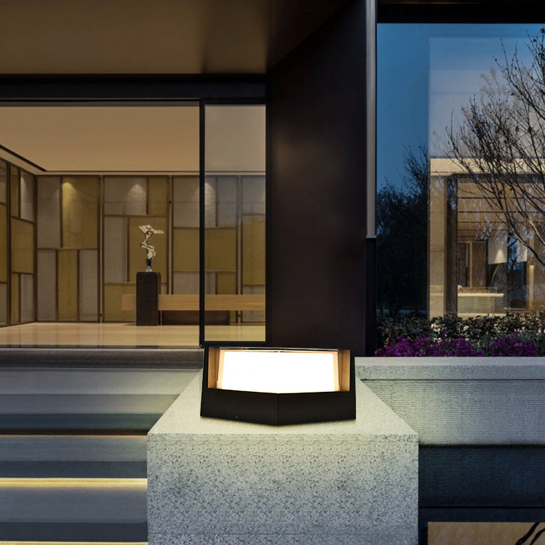 Black pentagon-shaped light glowing on a stone plinth outside a modern glass-fronted building at night. 3