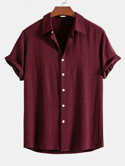 Short sleeve button-up shirt in deep burgundy on a wooden hanger, with white buttons down the placket. 7