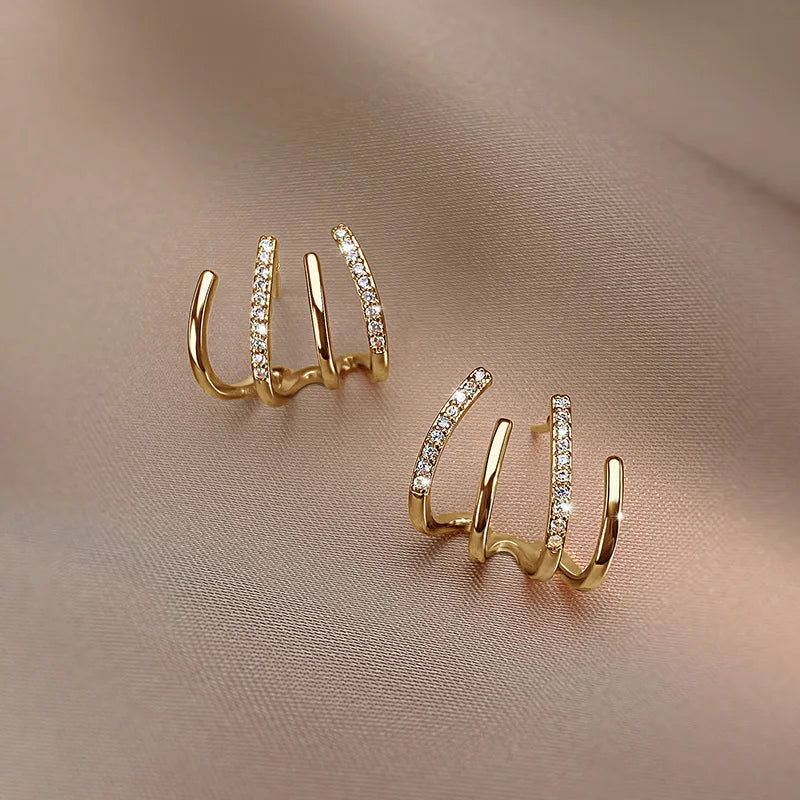 Pair of gold four-claw earrings with stone-set bars, laid flat on taupe fabric 9