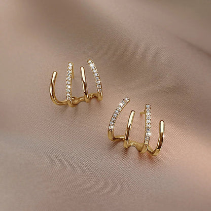 Pair of gold four-claw earrings with stone-set bars, laid flat on taupe fabric 9