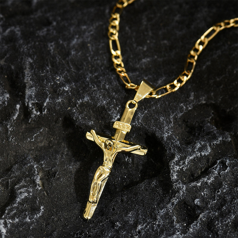 Gold crucifix pendant with INRI plaque and Figaro chain resting on dark textured rock 9