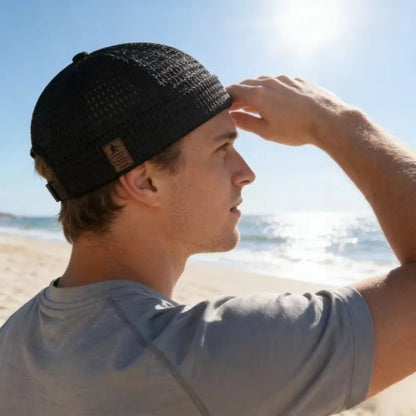 Man on a sunny beach seen from behind in the black mesh cap, shading his eyes 10