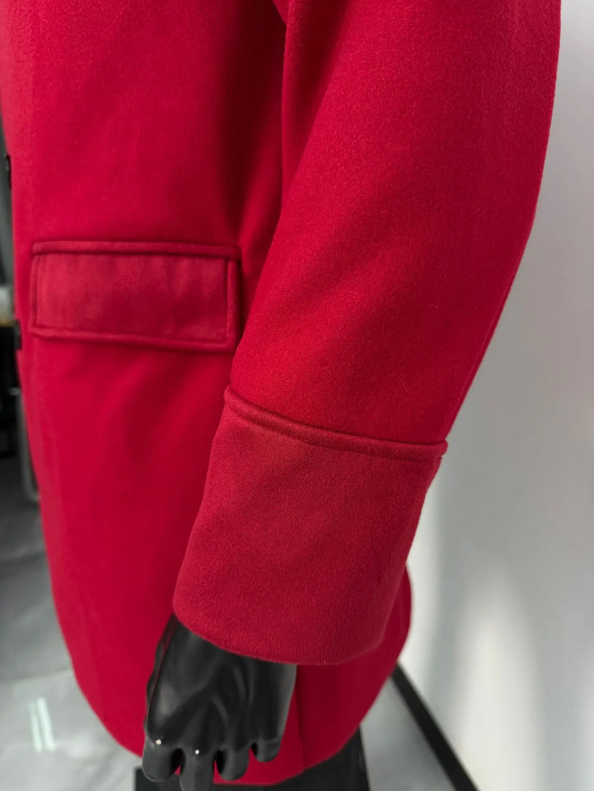 Close-up of the burgundy coat's flap pocket and turned-back cuff on a mannequin's arm 10