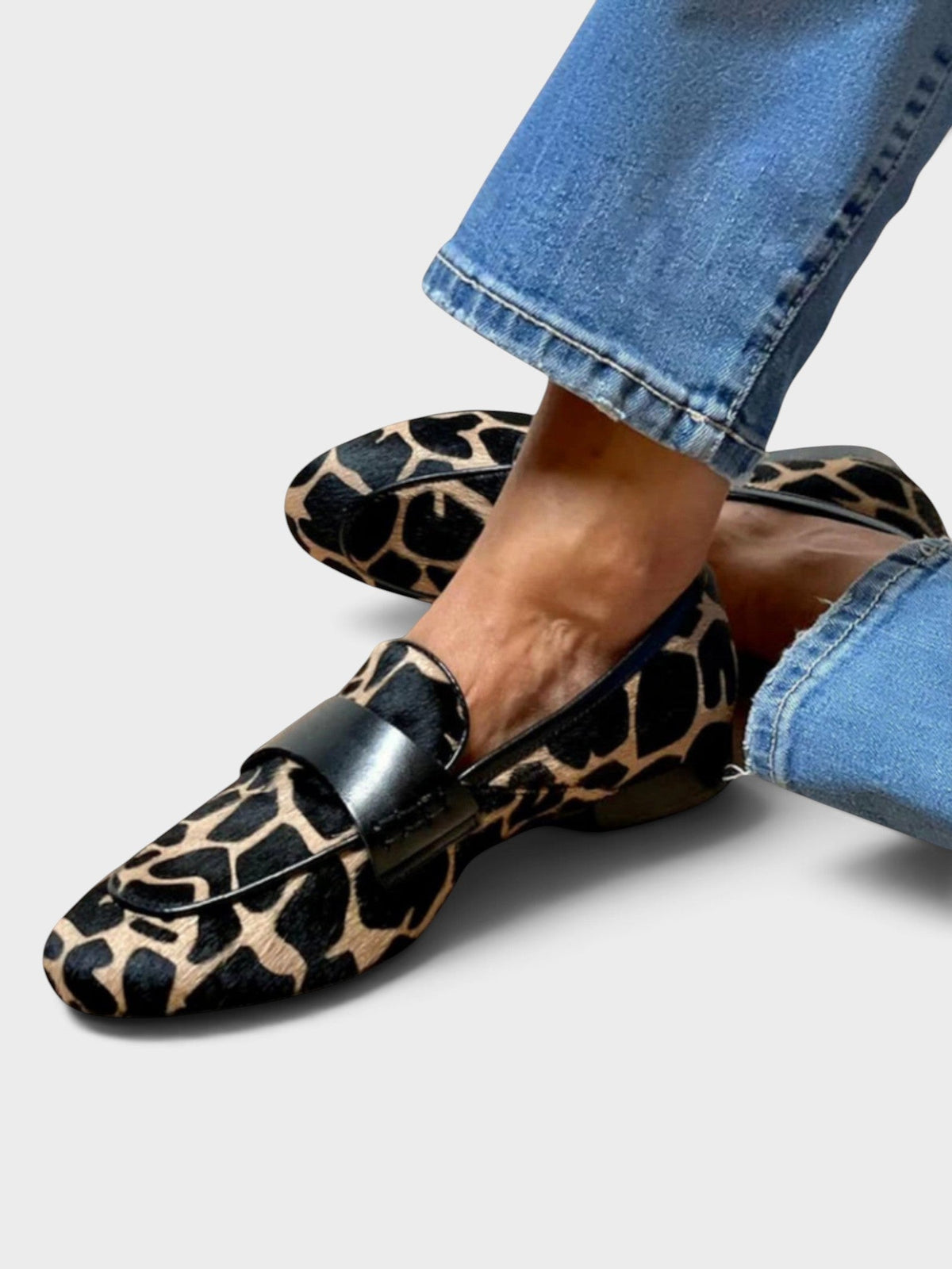 Worn with blue jeans, one foot crossed over the other, showing the loafers' black and tan animal print with black leather strap. 1