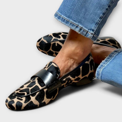 Close, slightly wider crop of the loafers worn with cuffed blue jeans, showing the black leather strap and animal print upper. 2