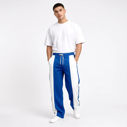 Studio shot of a model in blue sweatpants with white side panels, white tee and trainers 10