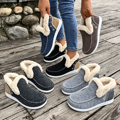 Five pairs of plush-lined slip-on trainers in navy, brown, black, charcoal and grey, arranged on wooden decking, some held by a model. 6