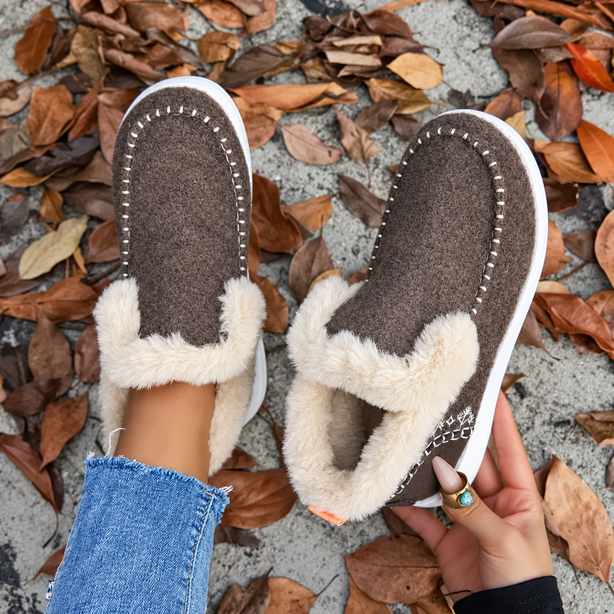 Overhead view of brown slip-on trainers with white stitching around the toe and fluffy cream lining, one worn and one held up. 8