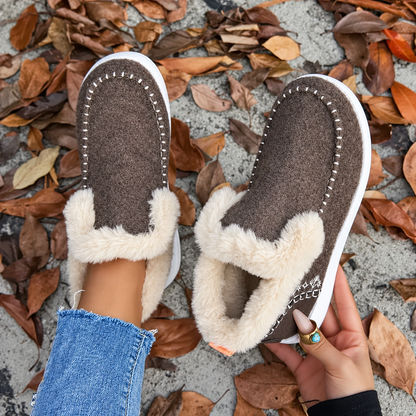 Overhead view of brown slip-on trainers with white stitching around the toe and fluffy cream lining, one worn and one held up. 8