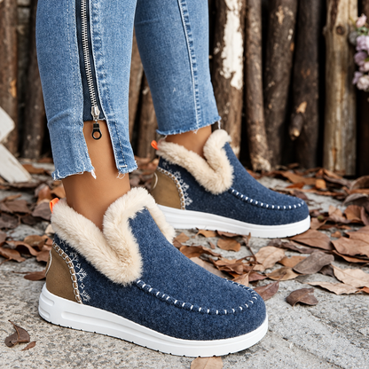 Navy slip-on trainers with plush cream collars, snowflake embroidery on tan heel panels and orange pull tabs, worn with zip-hem jeans. 10